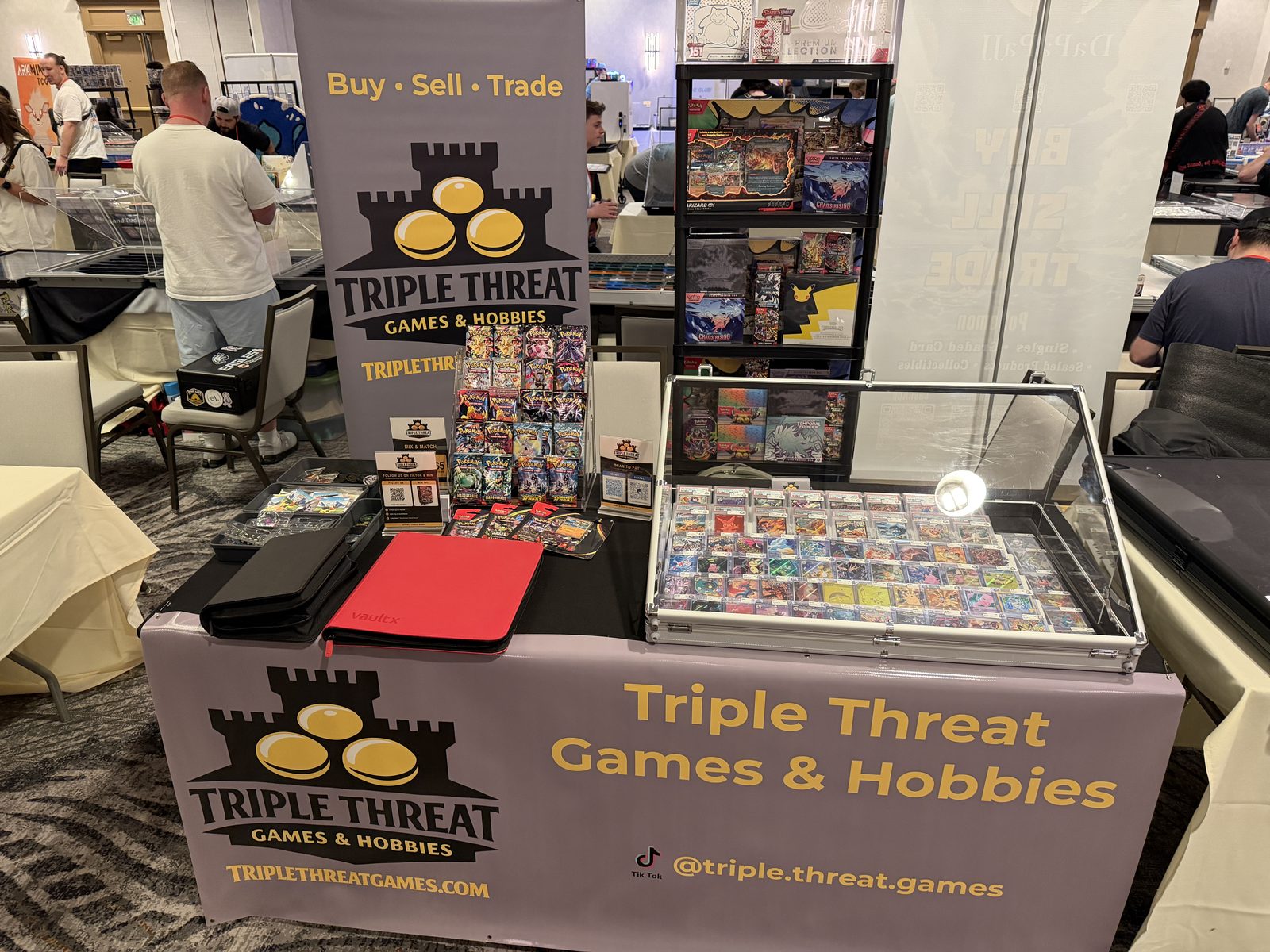 The Triple Threat Games & Hobbies booth at the Maximum Card Show, with graded cards, sealed product, and the company banner on display.
